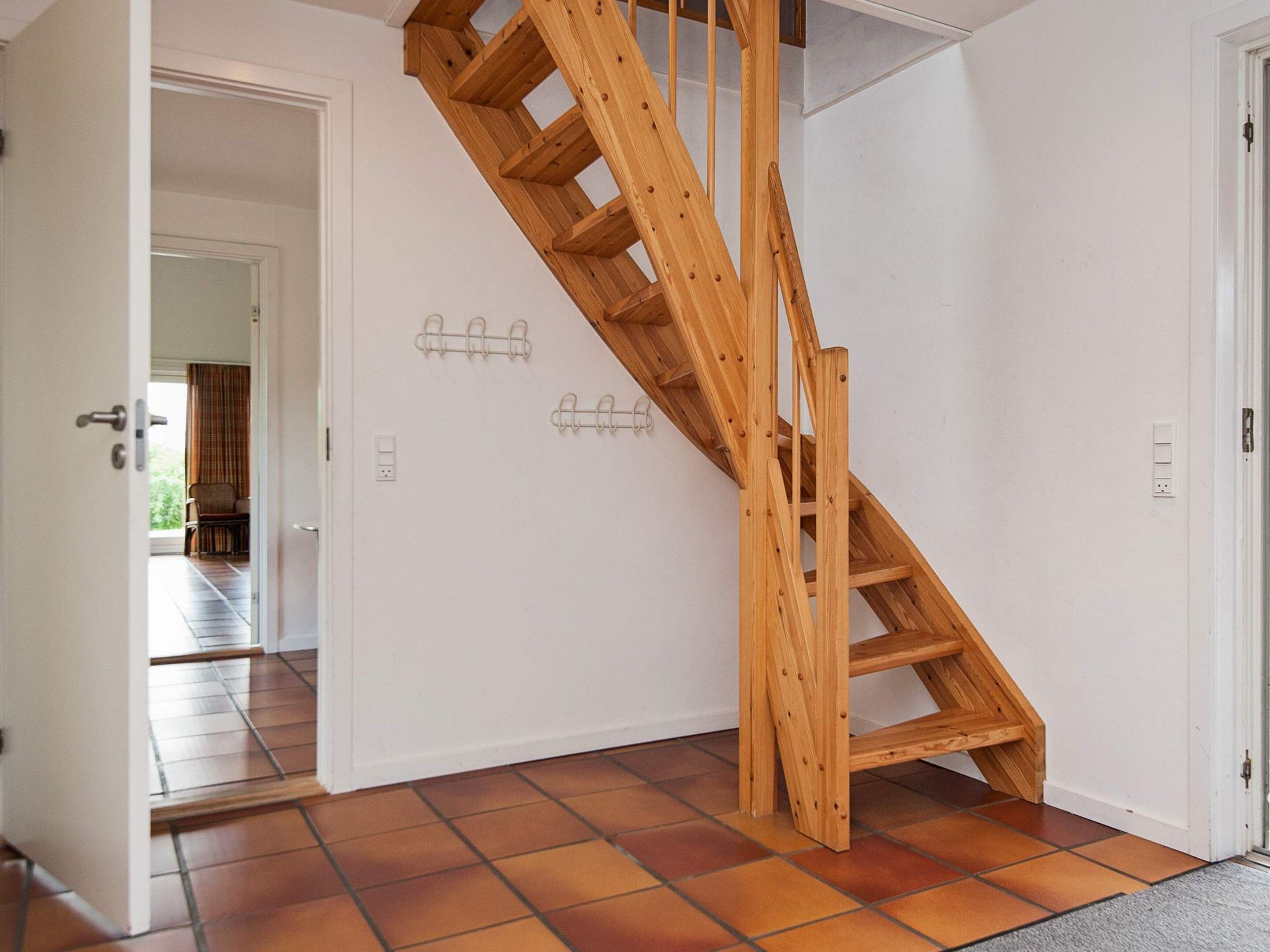 A wooden staircase in a room with white walls and a tiled floor.