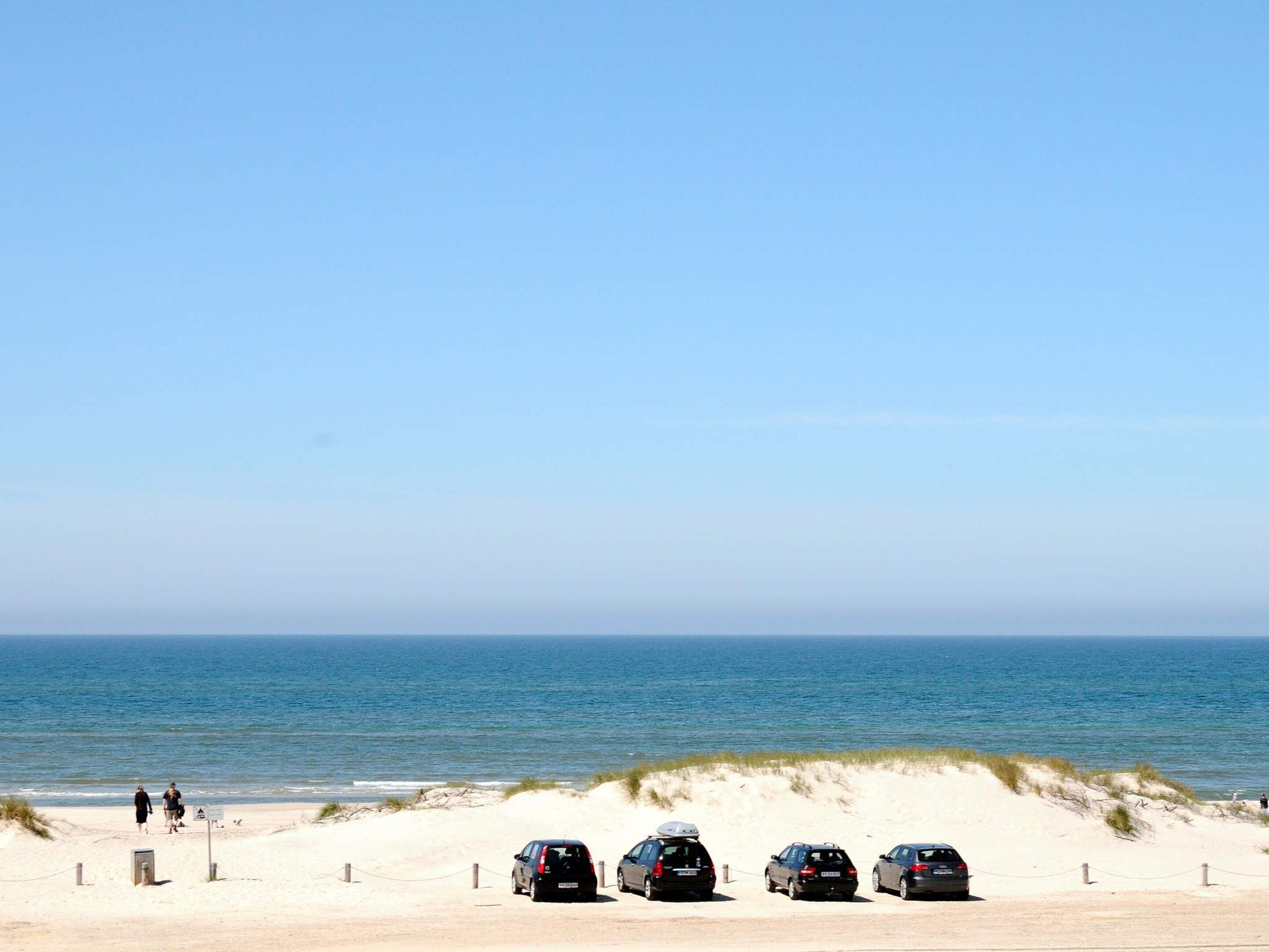 Una playa con cielo despejado, una zona arenosa y cuatro coches aparcados.