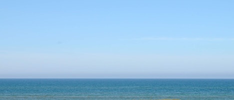 Uma praia com céu claro, faixa de areia e quatro carros estacionados.
