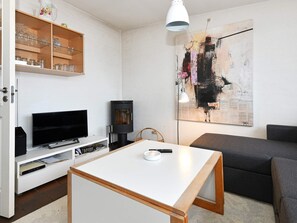 A modern living room with a flat-screen TV, a black wood-burning stove, a white coffee table, and a large abstract painting on the wall. - 4 Star Holiday Home in Henne (Henne)
