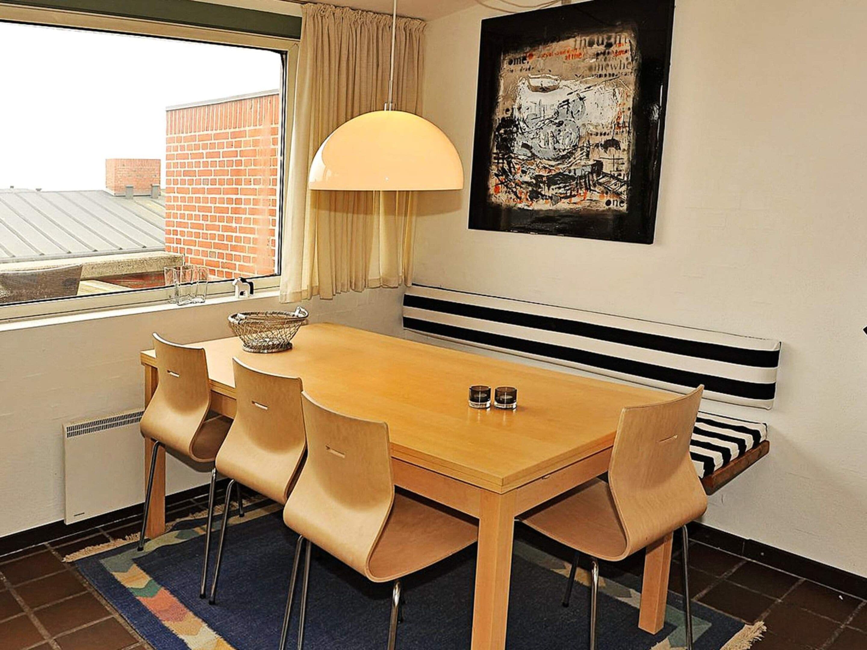 Un comedor con mesa de madera, cuatro sillas, una cesta y una lámpara colgante.