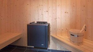 Een sauna met houten wanden, een zwarte sauna-oven en een houten emmer met een schuimspaan.