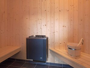 Ein Saunaraum mit Holzwänden, einem schwarzen Saunaofen und einem Holz-Eimer mit Wasserschöpflöffel.