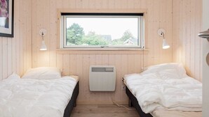 Een kleine kamer met twee bedden, een raam en een wandradiator.