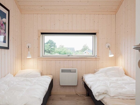 Ein kleines Zimmer mit zwei Betten, einem Fenster und einem Wandheizgerät.