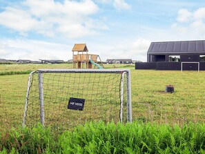 A soccer goal in a grassy field with a playground and a building in the background.