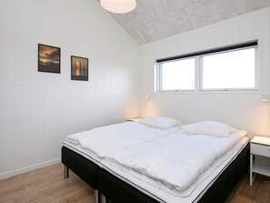 A bedroom with a bed, two wall-mounted pictures, a window, and a bedside table.
