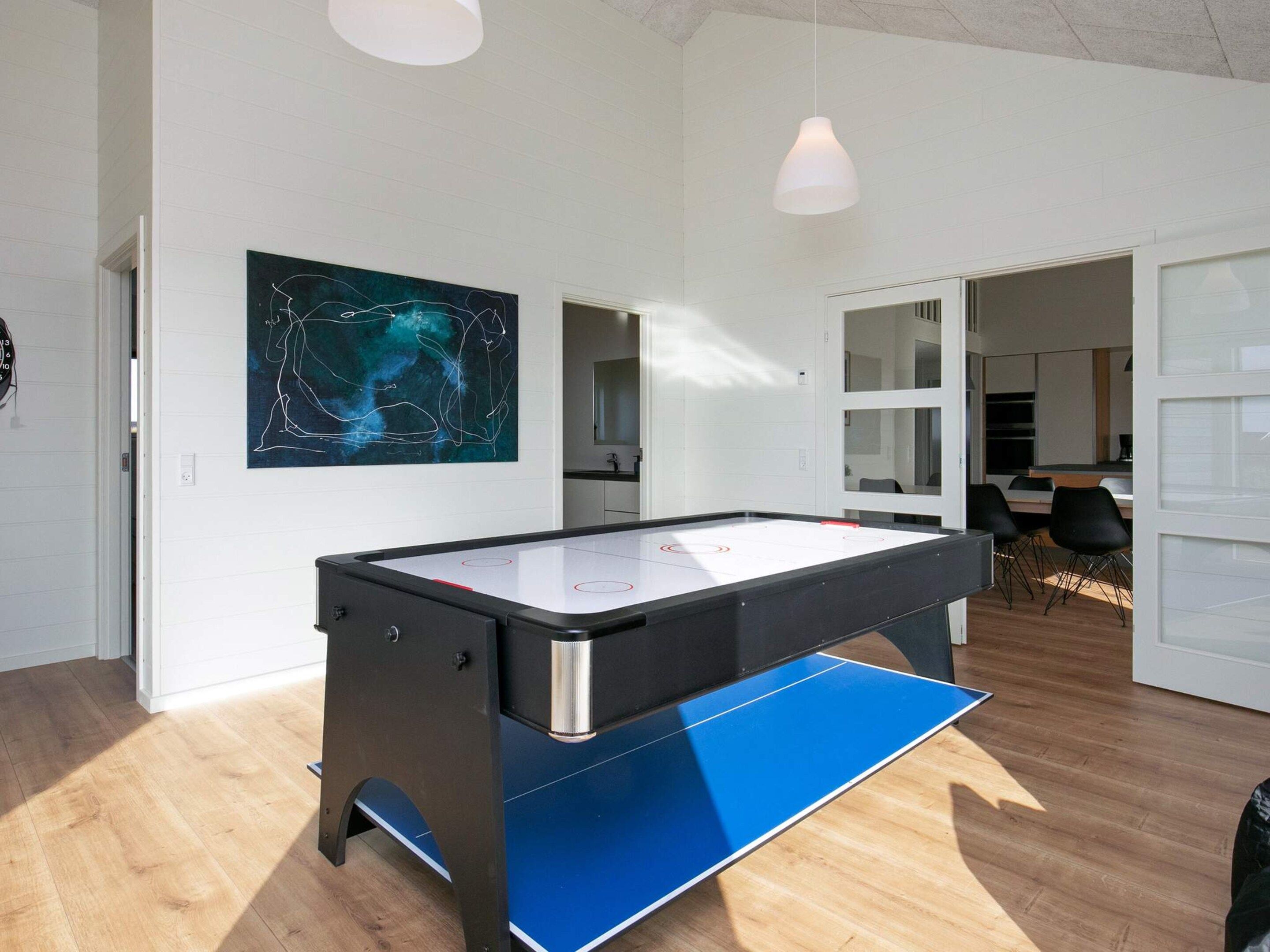 Une pièce moderne avec un baby-foot, un tableau au mur et un coin repas à l’arrière-plan.