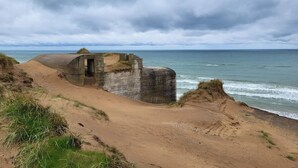 A coastal landscape with a sandy beach, a concrete structure, and the ocean under a cloudy sky. - 5 Star Holiday Home in Lokken (Lokken)