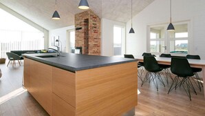 A modern kitchen with a central island, wooden cabinets, and pendant lighting. - 5 Star Holiday Home in Lokken (Lokken)