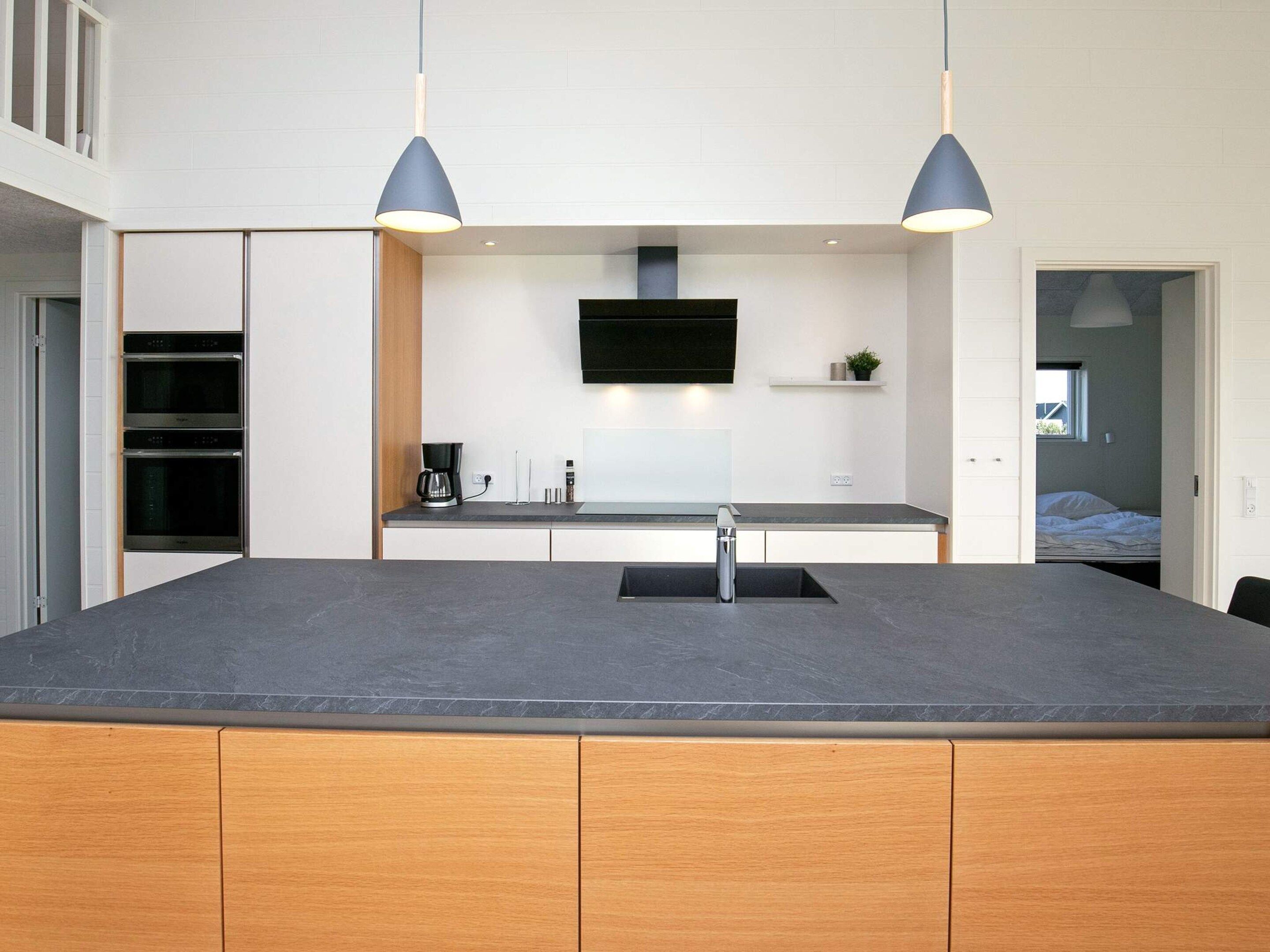 Une cuisine moderne dotée d’un îlot central, d’un four encastré et d’un téléviseur à écran plat fixé au-dessus du plan de travail.