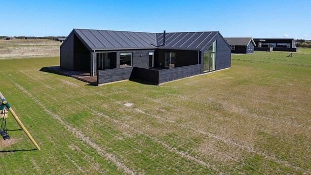 A modern, dark-colored building with a sloped roof, large windows, and a spacious outdoor area. - 5 Star Holiday Home in Lokken (Lokken)