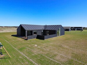 A modern, dark-colored building with a sloped roof, large windows, and a spacious outdoor area. - 5 Star Holiday Home in Lokken (Lokken)