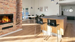A modern kitchen with a brick fireplace, wooden countertops, and a dining area with chairs. - 5 Star Holiday Home in Lokken (Lokken)
