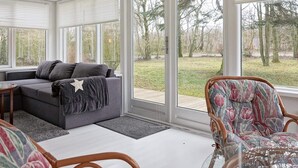 A sunroom with a grey sofa, a patterned armchair, and a glass coffee table. - 6 Person Holiday Home in Hasle-by Traum (Hasle)