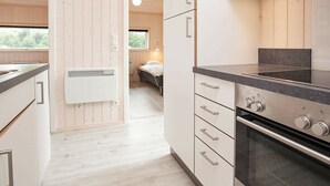 A modern kitchen with white cabinetry, a built-in oven, and a window overlooking a bedroom. - Holiday Home in Großenbrode (Grossenbrode)