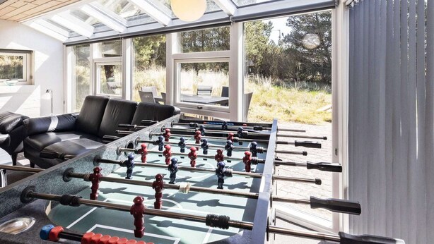 Ett rum med ett fotbollsspel, en svart lädersoffa och stora fönster med utsikt över omgivningarna.