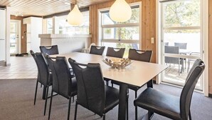 Ett rymligt matområde med ett stort bord och stolar, ett träpanelat tak och stora fönster som släpper in naturligt ljus.