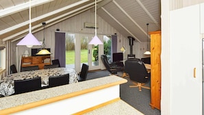 A cozy, well-lit room with a high ceiling, a dining area with a patterned table and chairs, a seating area with a sofa and chairs, and a view of the outdoors through large glass doors. - 8 Person Holiday Home in Oksbol-by Traum (Oksbol)