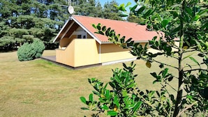 A small, single-story wooden cabin with a red roof, surrounded by a well-maintained lawn and dense trees. - 8 Person Holiday Home in Oksbol-by Traum (Oksbol)