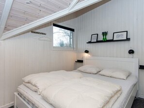 A bedroom with a sloped ceiling, a bed with white bedding, a window, and wall-mounted shelves with framed pictures and green bottles. - 6 Person Holiday Home in Hemmet (Hemmet)