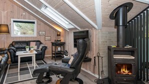 Una habitación acogedora con un sofá de cuero negro, un sillón reclinable negro, una mesita y un estufa de leña negra.