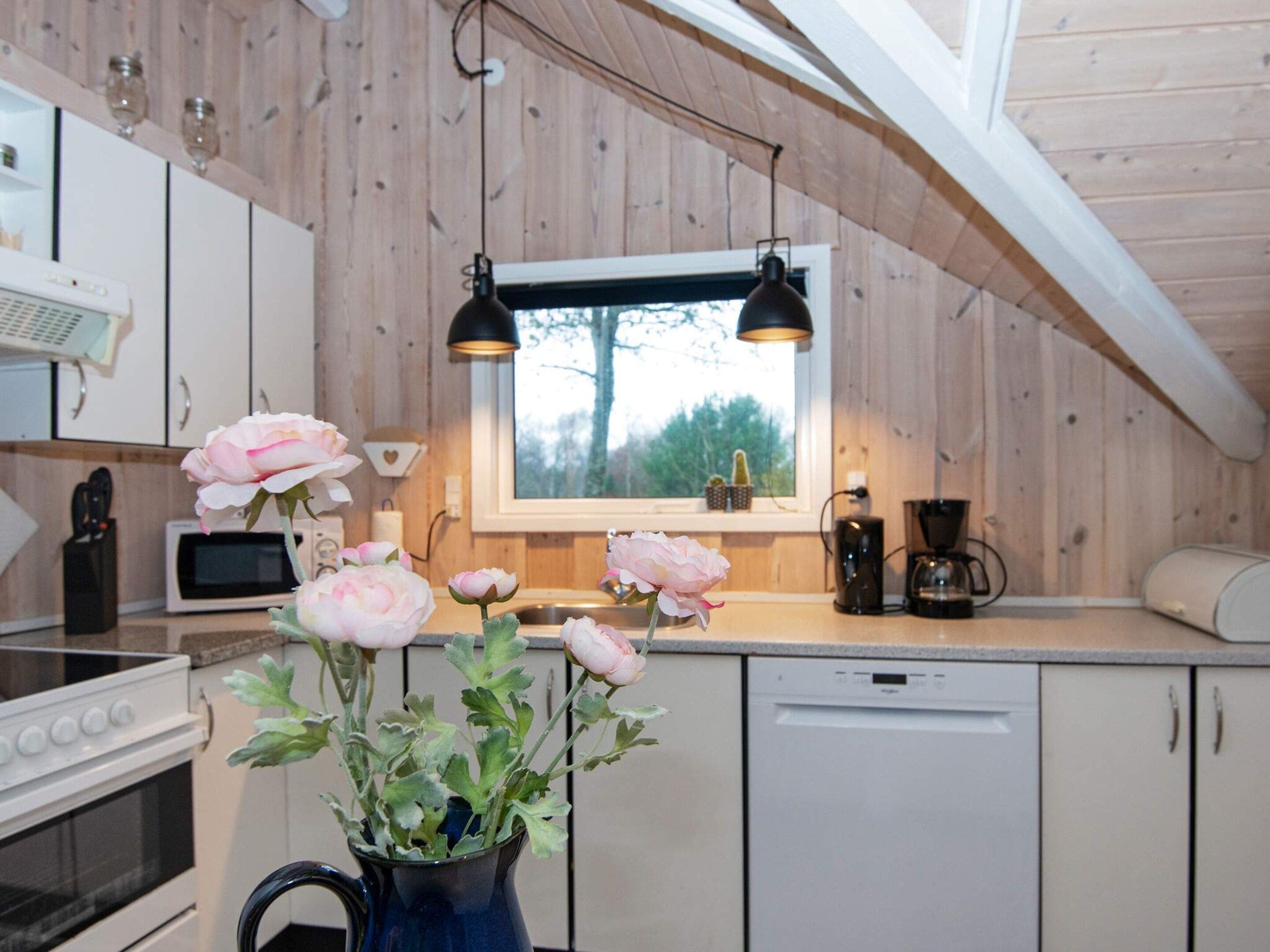 A kitchen with wooden walls, a window, and a vase with flowers.