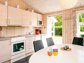 A modern kitchen with wooden cabinets, a stove, and a dining area with a table and chairs. - Entising Holiday Home in Jutland near Sea (Rømø)