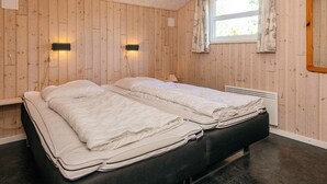 Ett rum med två sängar, träväggar, ett fönster med gardiner och väggmonterade lampor.