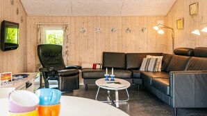 Ett mysigt vardagsrum med en lädersoffa, en svart fåtölj och ett litet runt bord med en fjärrkontroll och ljus.