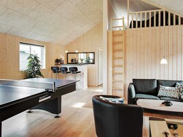 A room with a ping pong table, a sofa, a coffee table, a ladder, and a kitchen area with bar stools.