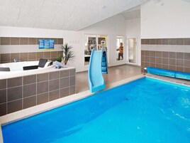 An indoor swimming pool with a slide, a reception area with a blue informational sign, and a person in the background.