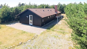 A small, single-story wooden building with a sloped roof, a door, and a chimney. - 8 Person Holiday Home in Blavand (Blavand)