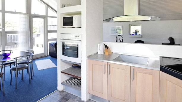 A modern kitchen with white cabinetry, a built-in oven, a microwave, and a stainless steel range hood. - 8 Person Holiday Home in Blavand (Blavand)