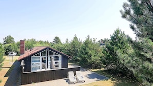 A small wooden cabin with a sloped roof, large windows, and a patio area with lounge chairs. - 8 Person Holiday Home in Blavand (Blavand)