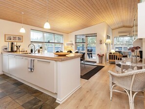 A modern kitchen with a central island, wooden ceiling, and large windows.