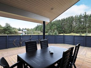 An outdoor patio with a table and chairs, surrounded by a wooden deck and a dark fence.