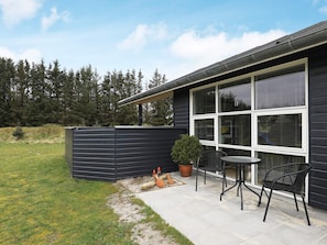 A modern house with a patio area featuring a table and chairs, a potted plant, and a wooden fence. - 5 Star Holiday Home in Lokken (Lokken)