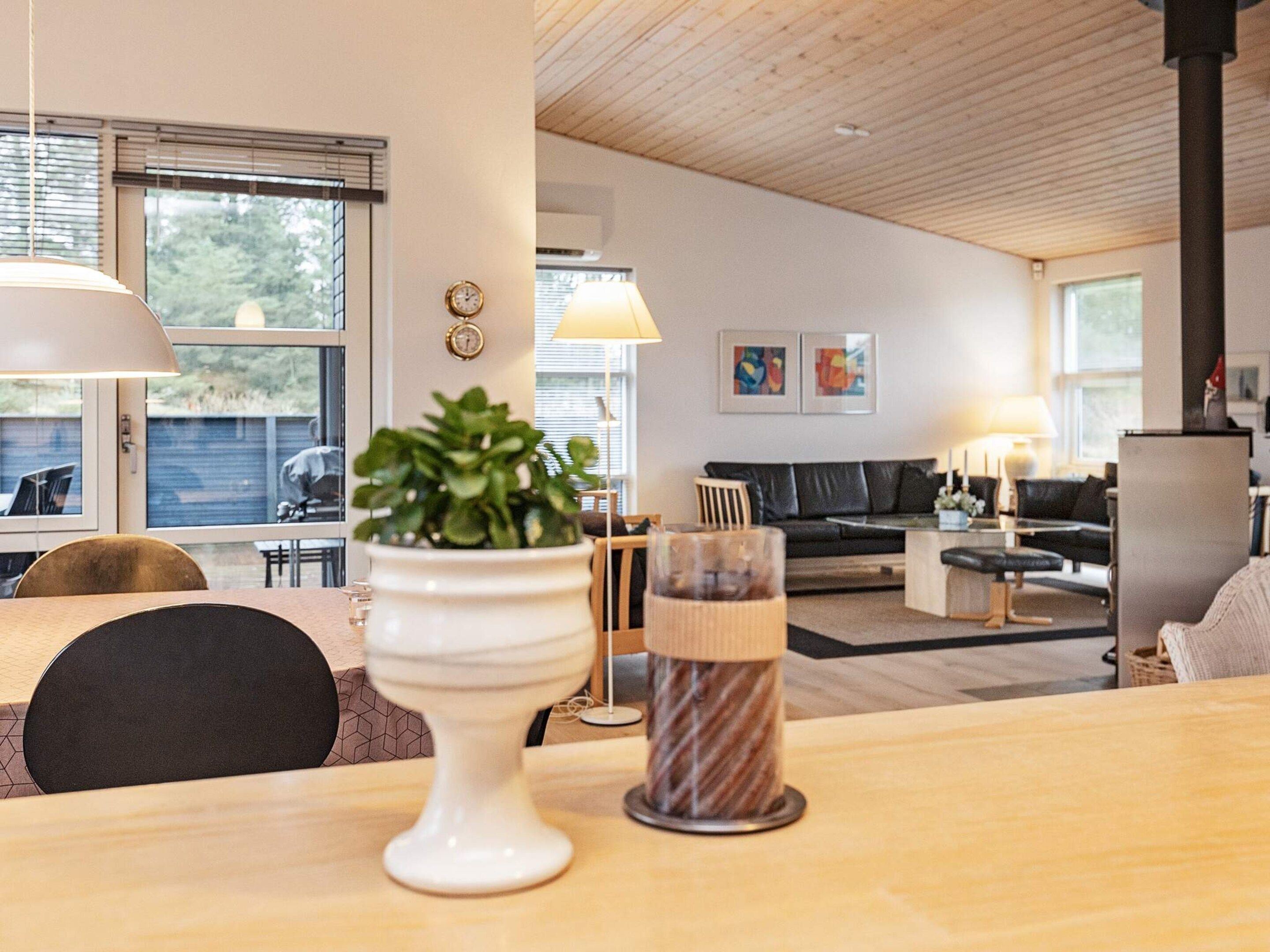 Ein modernes Wohnzimmer mit Essbereich, mit einem Holztisch, Stühlen, einer Topfpflanze und einer Lampe.