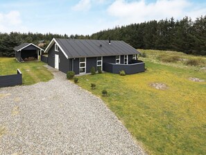 A modern house with a gravel driveway, a covered garage, and a fenced yard. - 5 Star Holiday Home in Lokken (Lokken)
