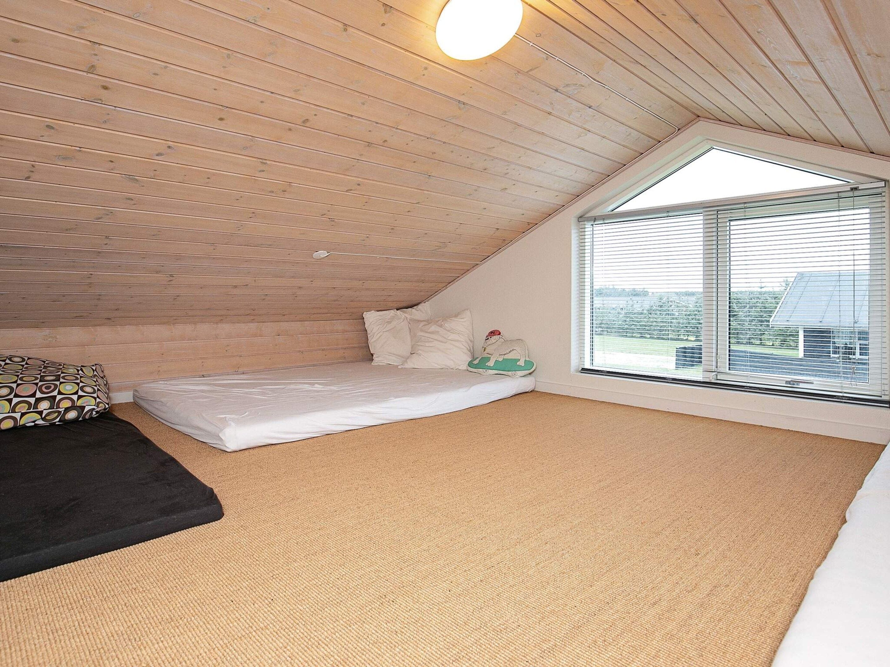 A small, sloped-roofed room with a single bed, a window, and a ceiling light.
