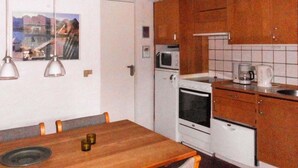 A compact kitchen with wooden cabinets, a white stove, a microwave, and a dining table with chairs. - Cozy Beach House in Blavand - By Traum Ferienwohnungen (Blavand)