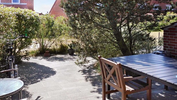 An outdoor patio area with a table and chairs, surrounded by potted plants and trees. - Cozy Beach House in Blavand - By Traum Ferienwohnungen (Blavand)