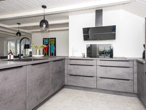 Uma cozinha moderna com armários cinzas, uma ilha grande, iluminação pendente e uma TV de tela plana na parede.