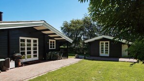 Ein Haus mit überdachter Terrasse, Rasen und einem kleinen Schuppen.