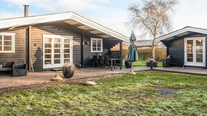 Ein Holzhaus mit überdachter Terrasse, Sitzgelegenheiten im Freien und einem großen Pflanzgefäß.