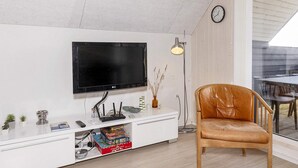 A modern living room with a flat-screen TV mounted on a white cabinet, a leather chair, a small table, and a dining area visible through a glass door. - 6 Person Holiday Home in Thisted-by Traum (Thisted)
