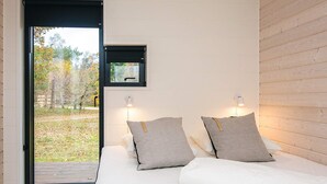A bedroom with a large window, two bedside lamps, and a view of a garden.