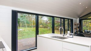 A modern kitchen with a large island, a built-in sink, and a view of the garden through large sliding doors.