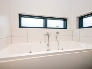 A modern bathroom with a freestanding bathtub, two showerheads, and two windows.